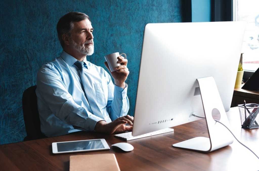 Accountant drinking coffee while working at a desktop computer